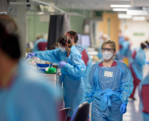 Busy hospital room with staff wearing full PPE