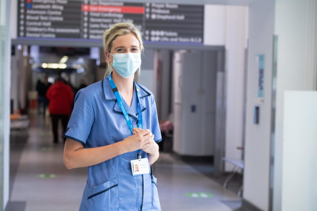 Female hospital worker in corridor smiling behind PPE