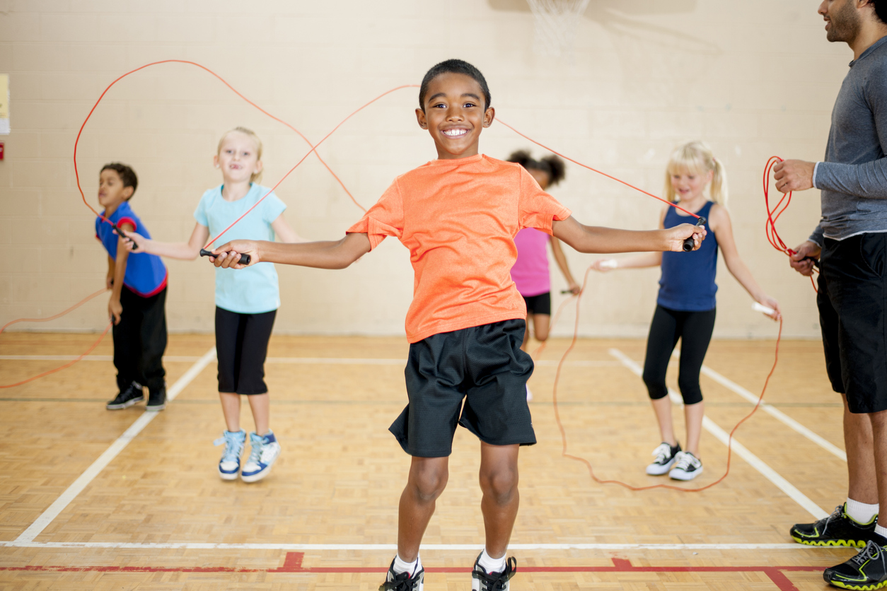 A multi-ethnic group of elementary age students in a gymnasium during physical education class, students are jumping rope inside the gym.
