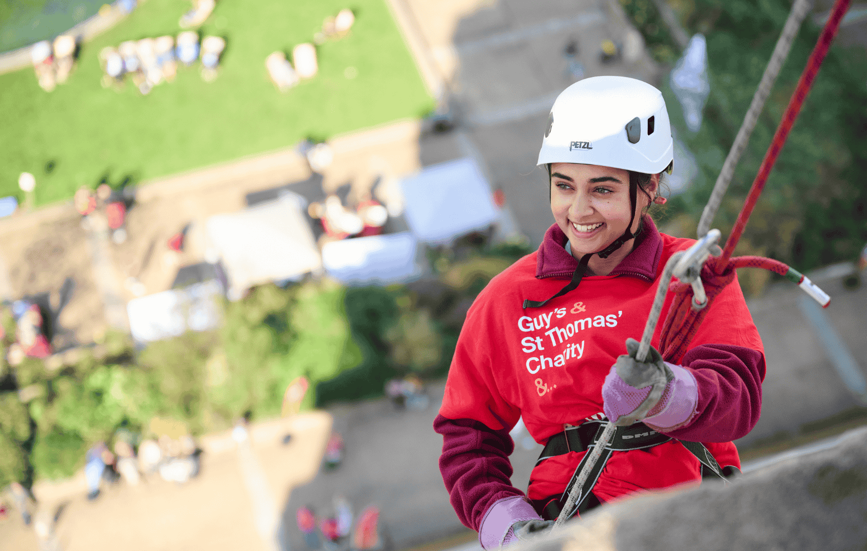 Woman appears to be smiling holding abseil rope, abseiling down St Thomas hospital with the hospital garden in the background below her.