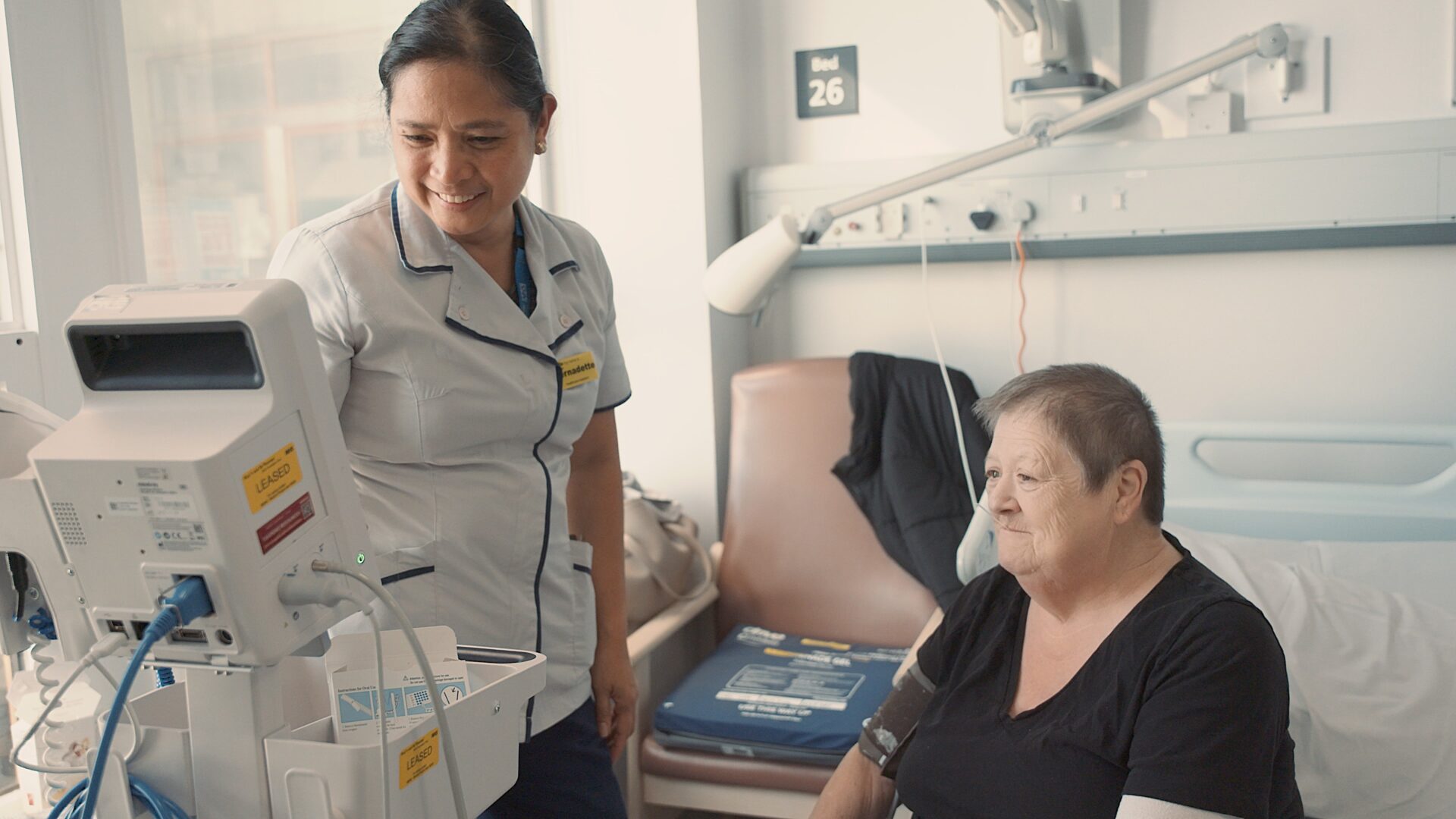 Nurse in the hospital measuring the patients blood pressure while she is sat on the bed.