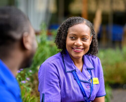 Portrait of NHS staff smiling in a garden where the hedges in the background are blurred.