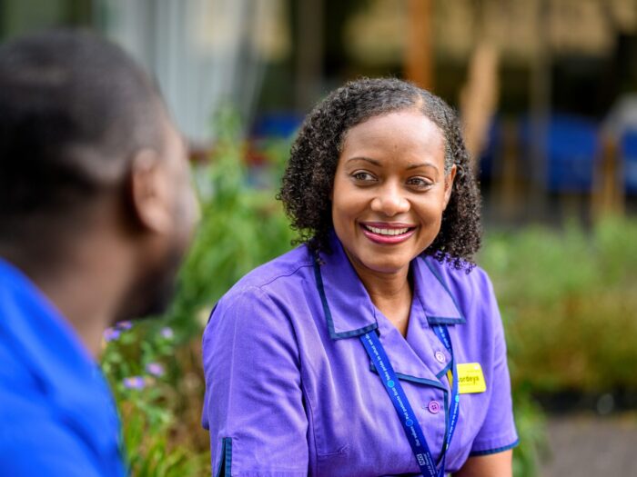 Portrait of NHS staff smiling in a garden where the hedges in the background are blurred.