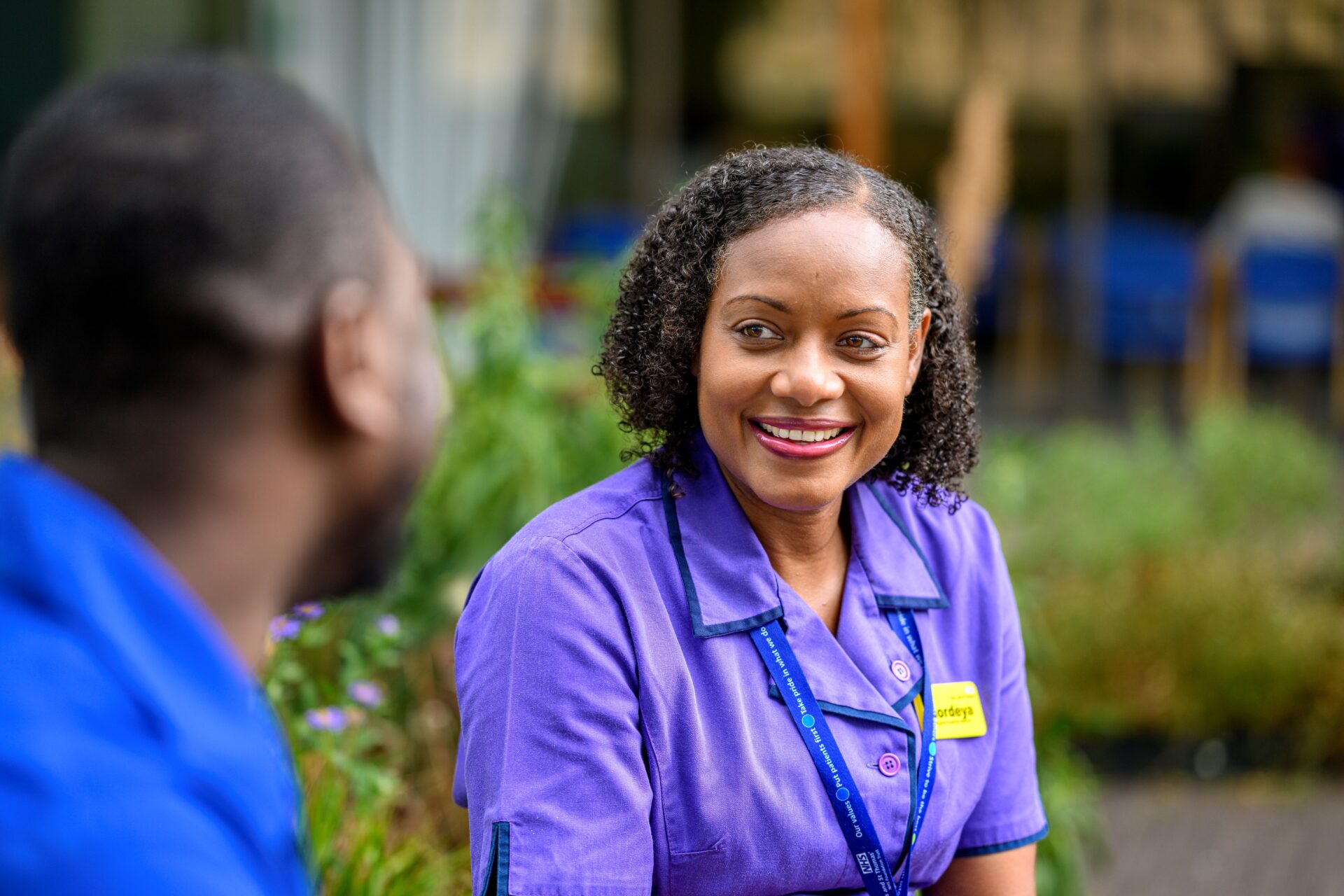 Portrait of NHS staff smiling in a garden where the hedges in the background are blurred.