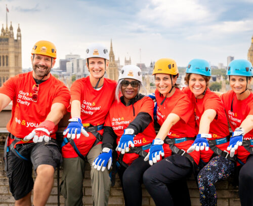 Abseilers on the roof of St Thomas hospital about to go down, with the skyline of London behind them.