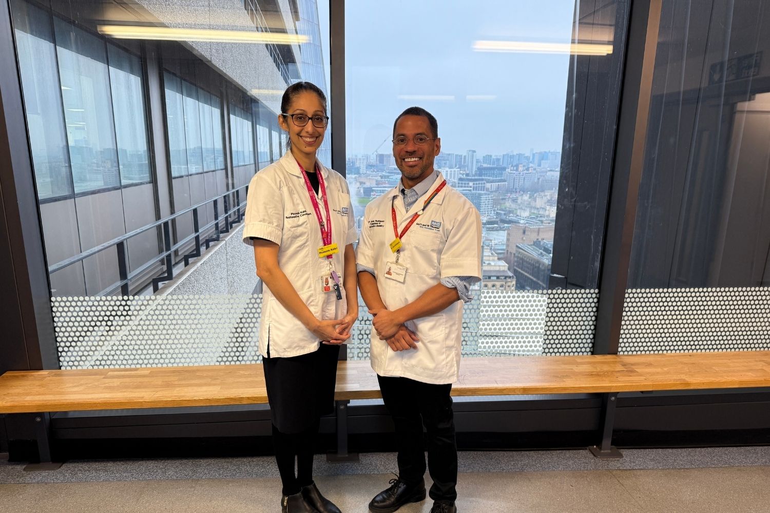 Poonam Kalsi and Jose Rodriguez leaders of the pilot project at Guy's hospital standing in their white uniform with lanyards in front of a window.