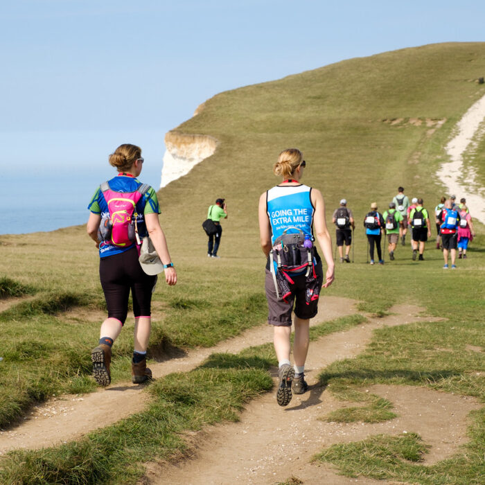 Ultra Challengers taking on the South Coast Ultra Challenge, the challengers are walking on a path, with the cliffs and sea in the background.