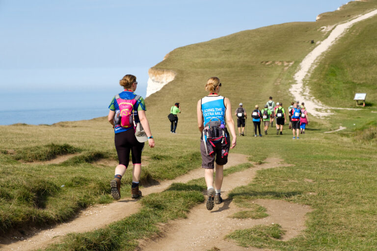 Ultra Challengers taking on the South Coast Ultra Challenge, the challengers are walking on a path, with the cliffs and sea in the background.