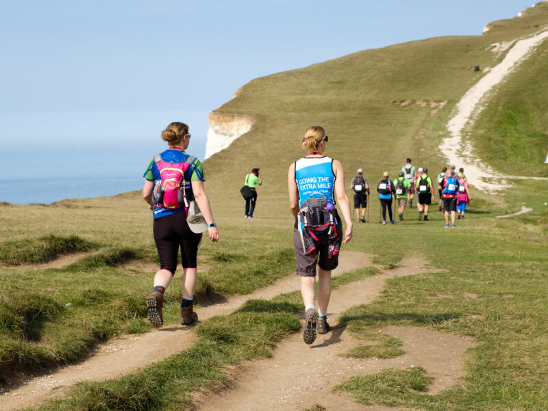 Ultra Challengers taking on the South Coast Ultra Challenge, the challengers are walking on a path, with the cliffs and sea in the background.
