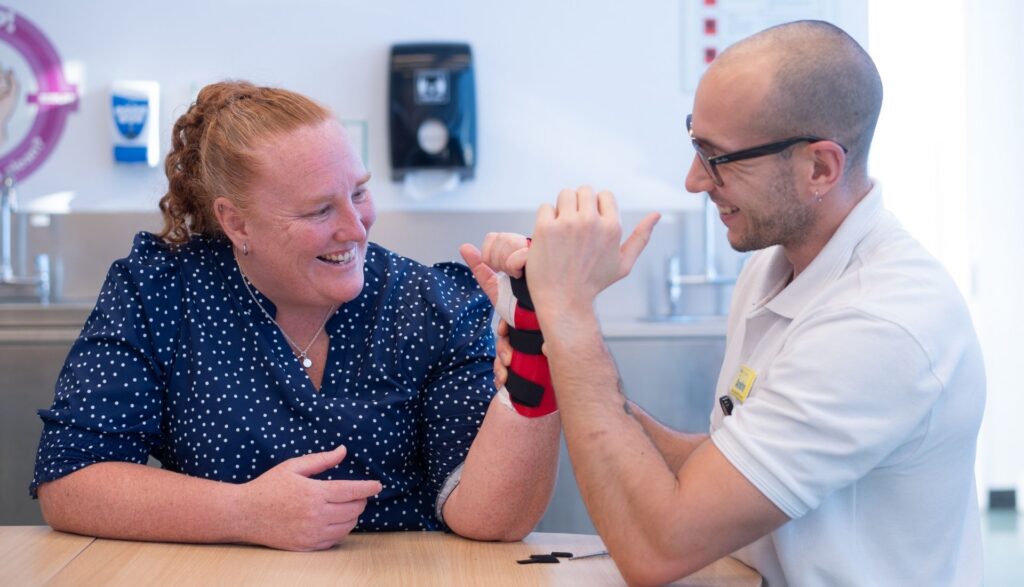 Patient Christy on the left in blue blouse appears to be smiling whilst her hand is being treated by Andre on the right.