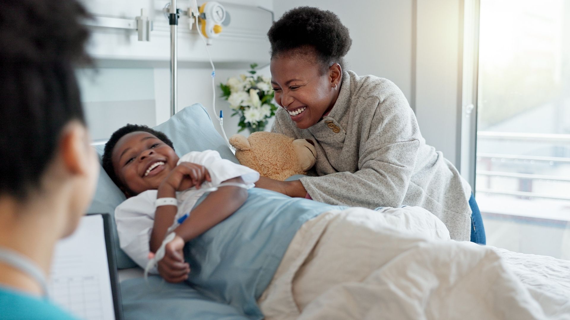 Child in hospital bed with his mum by his side, in front of them is a staff member giving them updates.